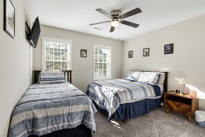A stylish and cozy bedroom featuring twin beds, a ceiling fan, and a peaceful ambiance.