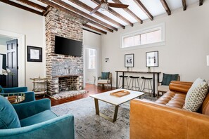 Unwind in style in this bright and airy living room featuring exposed beams, a cozy brick fireplace, and a plush mix of leather and velvet seating. Perfect for movie nights or morning coffee.