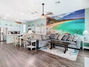 - Spacious open layout with a large beach mural that adds a serene coastal vibe
- Plush gray sectional and patterned pillows offer comfy seating for the whole group
- Full kitchen, dining set, and ocean toned decor perfect for gathering and relaxing