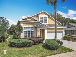 Inviting yellow toned home with double gables, sculpted hedges, and a pristine white garage set against a clear blue sky.