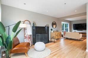 MAIN FLOOR:  A cozy nook with a sleek black fireplace, a caramel leather chair, and warm decor, perfect for reading or relaxing in a serene ambiance.