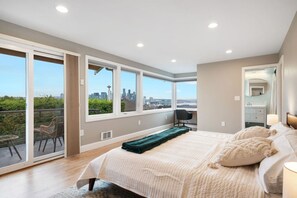 UPSTAIRS -MASTER BEDROOM & EN SUITE BATH: The master bedroom combines comfort and elegance, featuring a private patio with cozy seating and stunning Space Needle views, a dresser, smart TV, workspace, and a queen-size bed with a bedside lamp.