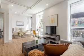 Airy, light-filled studio with a Smart TV lounge, cozy bed, and a bright workstation framed by downtown MTL mural views