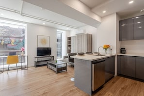 Spacious studio with open kitchen flow, cozy seating, and oversized windows offering a peek at downtown life