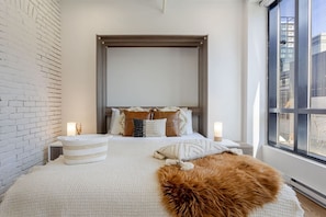 Soft neutrals and morning light define this cozy sleep setup with urban views and calming textures