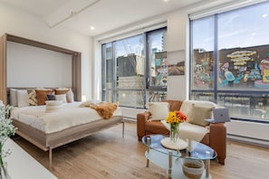 Murphy bed setup with plush bedding, leather accents, and abundant daylight from floor to ceiling windows