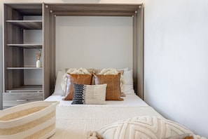 Neutral bedding, warm lighting, and built-in shelving create a snug retreat