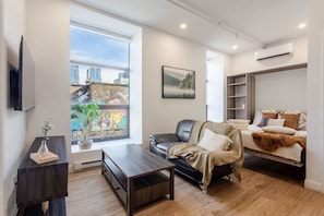 Open-concept living space with plush seating, Murphy bed, and plenty of light