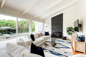 The airy living area features a vaulted ceiling with exposed beams, two plush oversized lounge suites, and a Smart TV for entertainment