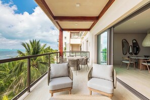 This image showcases a luxurious balcony with a breathtaking ocean view. The spacious outdoor area is elegantly furnished with comfortable seating and a dining table, perfect for relaxing or enjoying meals while surrounded by tropical greenery.