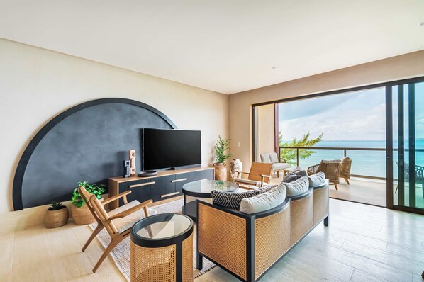 A stunning living space blending modern elegance with natural textures, featuring a breathtaking ocean view. The open design seamlessly connects the cozy indoor seating with a spacious balcony, inviting relaxation in a serene coastal setting.