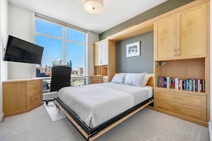 A multifunctional bedroom featuring built-in desks, floor-to-ceiling windows, a Murphy bed, and a spacious closet for ultimate efficiency.