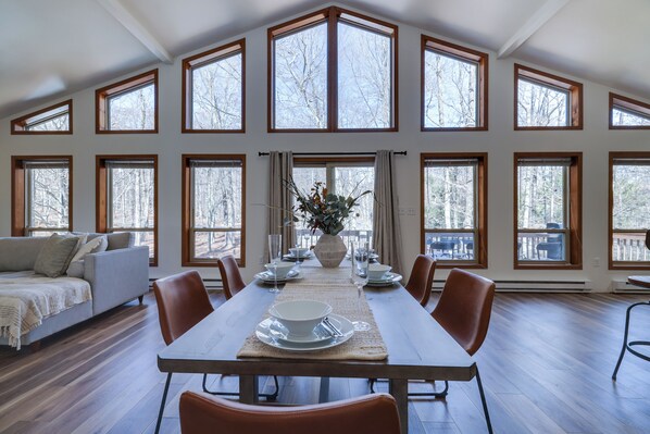 "Dine with a view! 🍽️🌿 This stunning open-concept dining area features soaring ceilings and floor-to-ceiling windows, flooding the space with natural light and breathtaking woodland views.