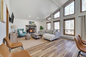 Cozy mountain retreat! 🔥🌲 This stunning living room features soaring ceilings, a warm stone fireplace, and floor-to-ceiling windows that bring in natural light and breathtaking woodland views.