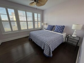 Elegant bedroom with rich wooden floors, cozy bedding, and plantation shutters for added privacy.