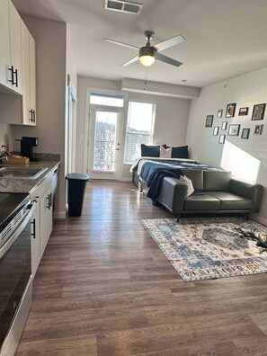 This open-concept space features a plush queen-size bed, stylish décor, a cozy seating area, and a fully equipped kitchen, all bathed in natural light.