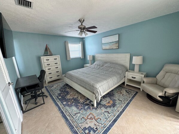 King-size bed with sheets, blanket, and pillows. Comfortable sitting chair.