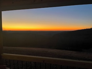 The sun dips below the mountains, casting a fiery glow across the landscape. A tranquil scene.