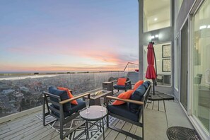 Experience breathtaking ocean views from this stylish balcony retreat, perfect for relaxing with a glass of champagne. Enjoy cozy outdoor seating, vibrant decor, and a serene sunset ambiance.
