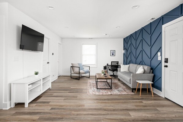 Welcome to the living area of the modern carriage house! Discover a striking navy blue accent wall, which adds a touch of sophistication and serves as a bold backdrop to the space.