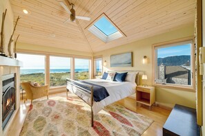 Master bedroom with ocean view, desk work space, gas fireplace, king bed, sitting chair, and TV with Direct TV and streaming.
