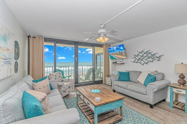 The oceanfront living room features a cozy queen sofa sleeper with stunning ocean views. A sliding glass door opens to the balcony, inviting fresh sea breezes and natural light. Relax in a coastal-inspired space where the beach is just steps away.