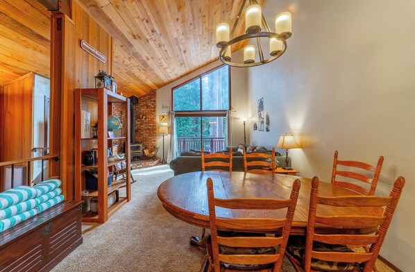 Bright open living area with vaulted ceilings and pine tree forest view.