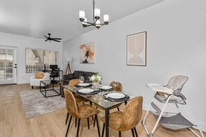 Dining area, seats 4, high chair Modern living room with accent wall, dedicated working space, TV, plush couch, and sofa bed