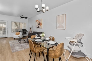 Dining area, seats 4, high chair Modern living room with accent wall, dedicated working space, TV, plush couch, and sofa bed