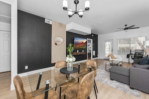 Dining area, seats 4, high chair Modern living room with accent wall, dedicated working space, TV, plush couch, and sofa bed