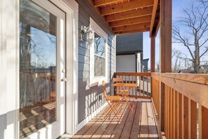 Sunny porch with wood deck, orange bistro set, and peaceful neighborhood views.
