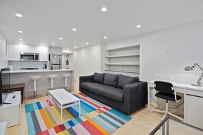 Relax into the cozy living area, complete with a bold pop of color, open shelving, and a handy desk for whatever the day brings