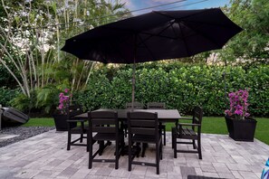 Enjoy meals in the fresh air at this inviting outdoor dining space, complete with a large table, comfortable seating, and a shady umbrella.