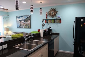 The kitchen is convenient and accessible to the living room with beach-themed decor and hanging lights!