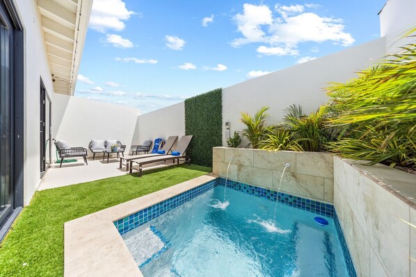 A serene outdoor oasis featuring a refreshing plunge pool, surrounded by lush greenery and comfortable lounging chairs, perfect for relaxation under the bright blue sky.