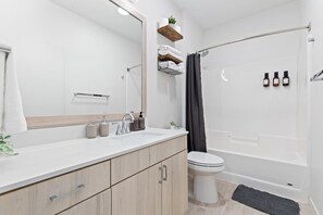 This bright and welcoming bathroom invites you to freshen up in comfort. Enjoy the forest-inspired shower curtain that adds a calming touch to your routine, complemented by the cozy rug underfoot and sparkling clean fixtures.