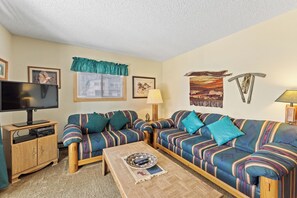 Living area with a wood burning fireplace, workspace, queen sleeper sofa, and balcony access.