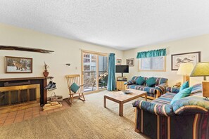 Living area with a wood burning fireplace, workspace, queen sleeper sofa, and balcony access.