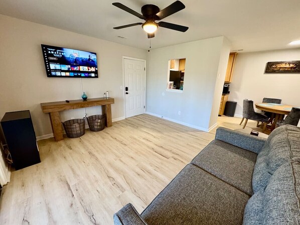 Spacious living area with a mounted TV, stylish console table, cozy sofa, ceiling fan, and dining space.