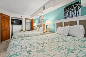 A vibrant beach cove room with brilliant colors, two cozy queen beds, a smart TV, and a spacious chest of drawers. A closet offers extra storage, while the bright decor creates a cheerful, relaxing vibe perfect for a coastal retreat.