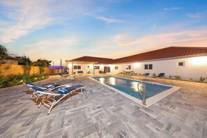 Sunset poolside view with lounge chairs.



