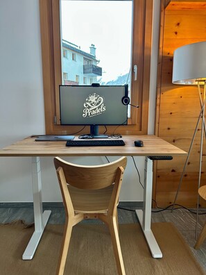 Height-adjustable work table with 27" 5K screen, webcam, headset, charging cable, keyboard, mouse