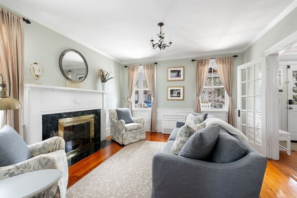 This formal living room features a fireplace (non-functional) with a classic black marble finish, plush armchairs, and large windows that bathe the space in natural light.