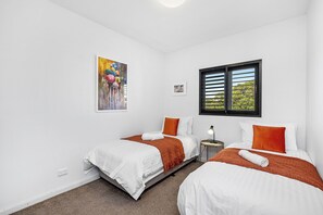 Retreat to a cozy twin bedroom, where two comfortable single beds await, each adorned with crisp white linens and vibrant orange accents. 