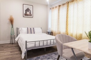 A Philly apartment bedroom with sleek vibes. Large window floods the space with light, highlighting a TV, bed & workstation. #SereneSleep