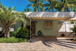 A tropical, palm-lined entryway leading to Unit B's private entry, with a paved driveway and lush landscaping, offering a peaceful retreat just steps from the water.