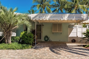 A tropical, palm-lined entryway leading to Unit B's private entry, with a paved driveway and lush landscaping, offering a peaceful retreat just steps from the water.