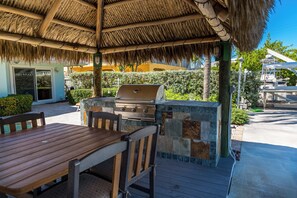 A covered dining area under the tiki hut with a built-in gas grill, ideal for barbecues and waterfront meals.