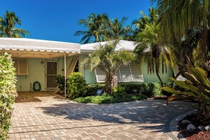 A tropical, palm-lined entryway leading to Unit A's private entry, with a paved driveway and lush landscaping, offering a peaceful retreat just steps from the water.