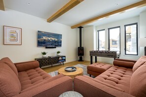 Custom Gas Fireplace In The Living Area, With A Wall Mounted 65" HD TV and Foosball Table